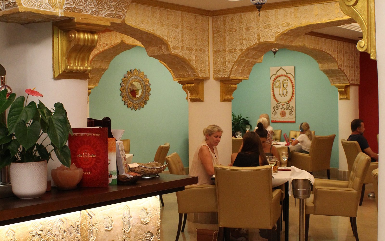 The dining room at Mini India Elviria — gold mughal arches and teal alcoves